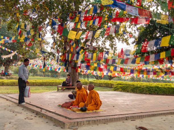 Monks under prayer flags in Lumbini Lumbini, Nepal - March 2015: Buddhist monks sitting under a tree covered with colourful prayer flags in Lumbini. lumbini nepal stock pictures, royalty-free photos & images