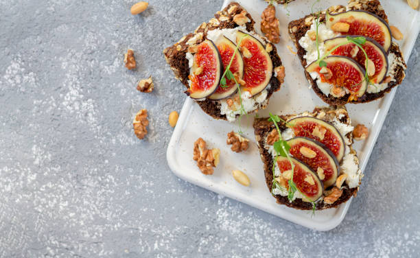 istock Toast with figs, cheese, honey, herbs and nuts. Delicious breakfast on white board top view 1273509972