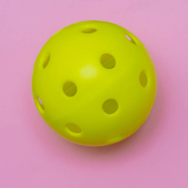 istock Bright yellow pickleball or whiffle ball on a solid bright pink flat lay background symbolizing sports and activity with copy space. 1273513884