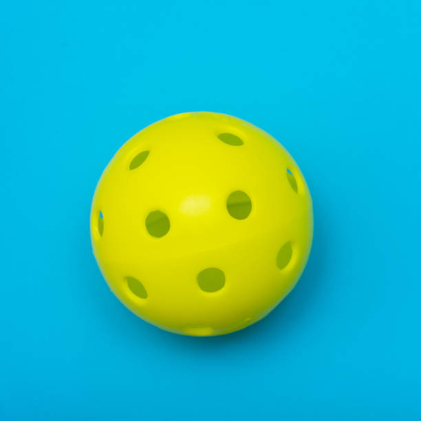 Bright yellow pickleball or whiffle ball on a solid aqua blue flat lay background symbolizing sports and activity with copy space. stock photo