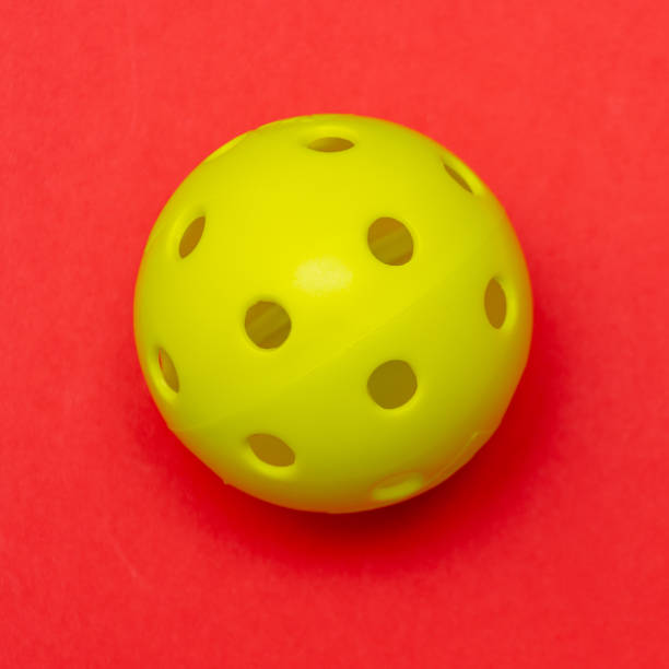 istock Bright yellow pickleball or whiffle ball on a solid bright red flat lay background symbolizing sports and activity with copy space. 1273513905