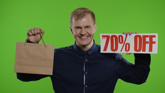 Shocked happy man showing shopping bags and Up To 70 Percent Off inscriptions signs. Good holiday discounts, low prices for shopping. Studio shot on chroma key background. 6k downscale, slow motion