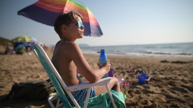 Little boy on beach drinking from reusable water bottle.