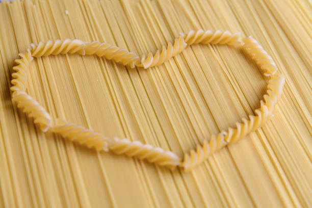 Raw uncooked fusilli pasta (also known as rotini) lies in heart shape on raw spaghetti pasta. Abstract food background. Selective focus. Copy space for your text. Italian cuisine theme.