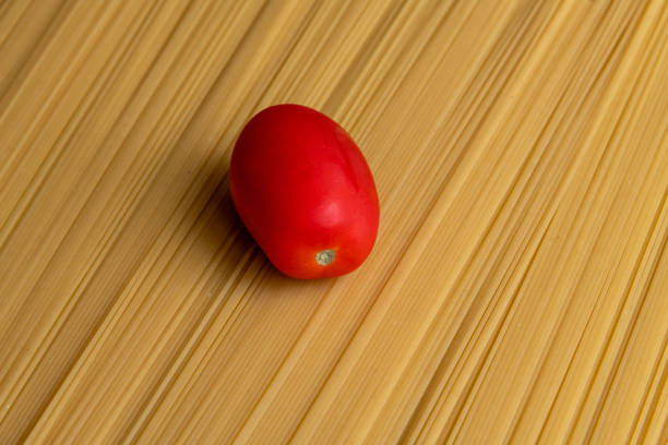 Fresh red plum tomato lies on raw uncooked spaghetti pasta made from milled durum wheat. Abstract food background. Selective focus. Copy space for your text. Italian cuisine theme.
