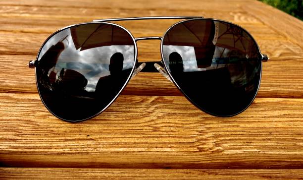 istock Sunglasses with silhouette reflection on wooden table 1273520527