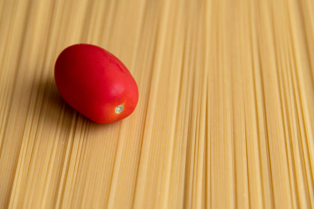 Fresh red plum tomato lies on raw uncooked spaghetti pasta made from milled durum wheat. Abstract food background. Selective focus. Copy space for your text. Italian cuisine theme.
