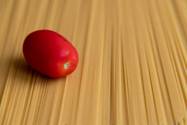 Fresh red plum tomato lies on raw uncooked spaghetti pasta made from milled durum wheat. Abstract food background. Selective focus. Copy space for your text. Italian cuisine theme.