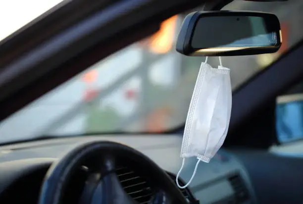 white medical mask hanging in the rearview mirror of the car