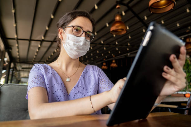 istock Young woman with face mask, using tablet at restaurant 1273525416