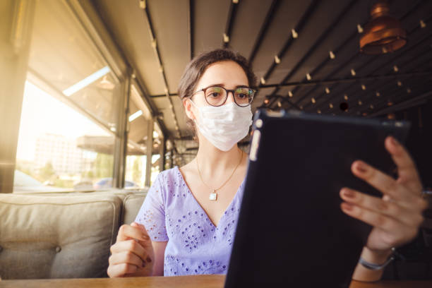 istock Young woman with face mask, using tablet at restaurant 1273525429