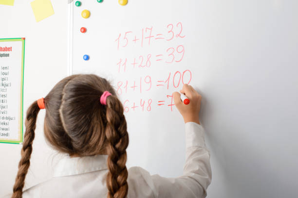 istock Clever female learner of primary school writing on board some mathematical equations, counting numbers 1273529926