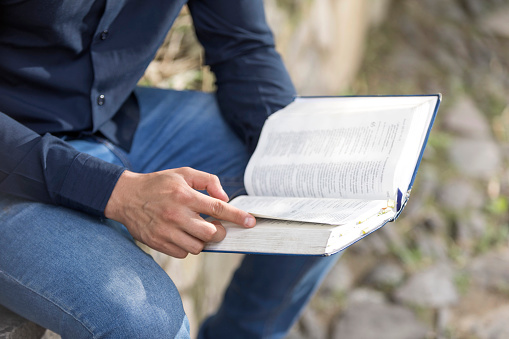 Young businessman reading the Sacred Bible in outdoor garden