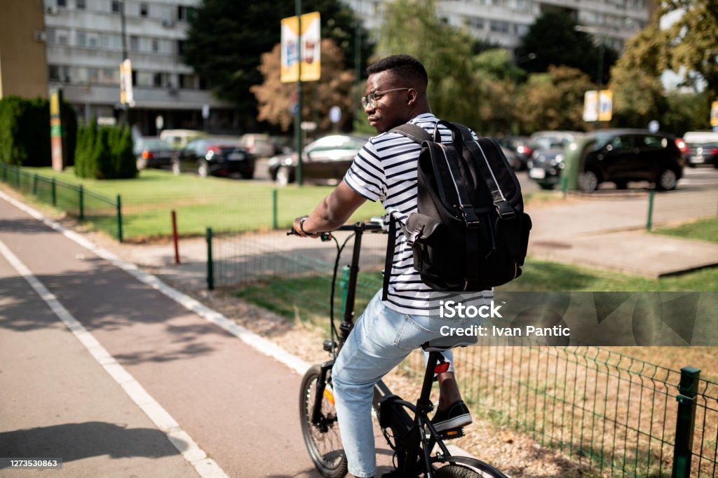 Rear view of a young African American male student riding a bicycle Rear view of a handsome young African American male student taking an electric bicycle to class, carrying a backpack Cycling Stock Photo