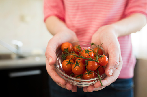 Close-up of a young woman holding bowl full with cherry tomato in the kitchen at home