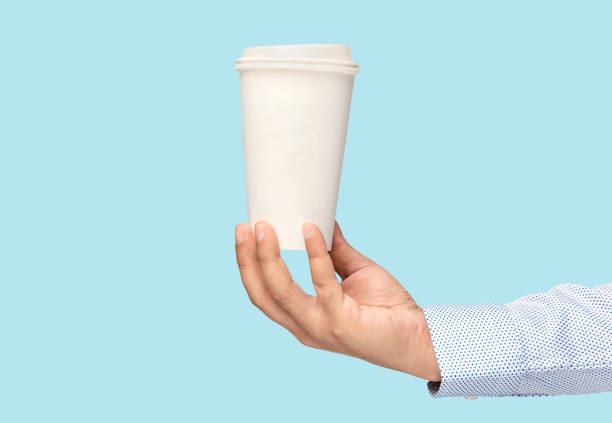 istock Man holding out a paper cup of coffee on blue background 1273531279