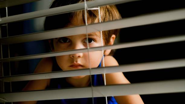 istock pensive little boy peeking through a window at night 1273540405