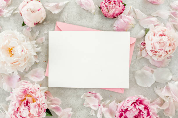 istock Mockup invitation, blank paper greeting card, pink envelope and peonies on gray stone table. Flower background. Flat lay, top view 1273543123