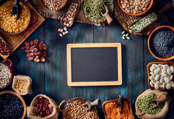 immagine low key vista dall'alto di una grande varietà di fagioli secchi girati dall'alto su un tavolo di legno rustico con una lavagna vuota con spazio di copia - legume bean chick pea sack foto e immagini stock