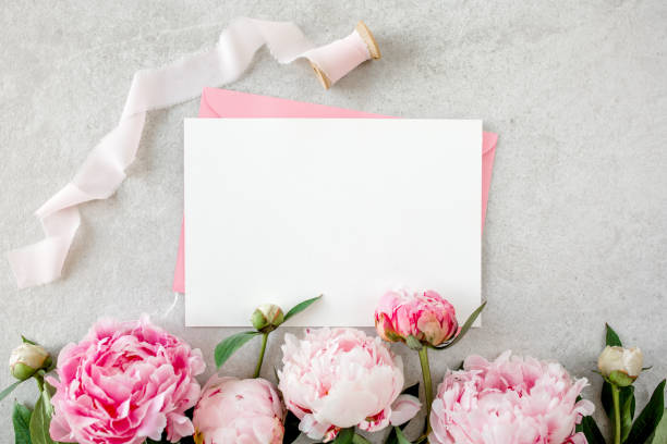 istock Mockup invitation, blank paper greeting card, pink envelope and peonies on gray stone table. Flower background. Flat lay, top view 1273545097
