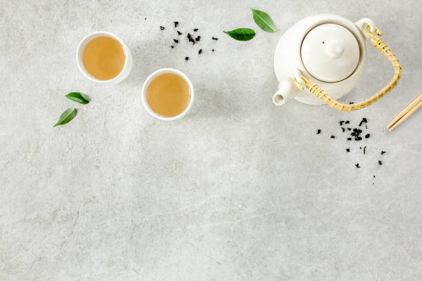 istock Herbal tea with two white tea cups and teapot, with green tea leaves. Flat lay, top view. Tea concept 1273548377
