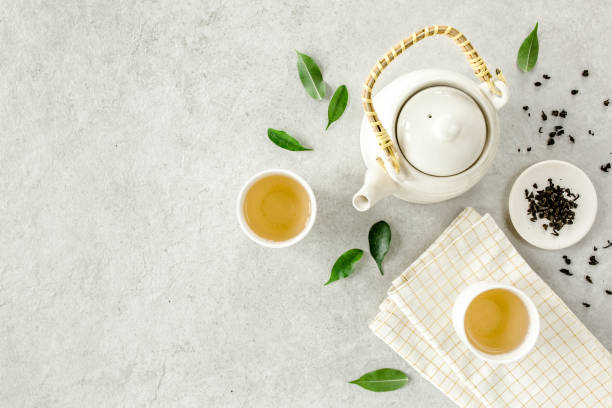 istock Herbal tea with two white tea cups and teapot, with green tea leaves. Flat lay, top view. Tea concept 1273549045