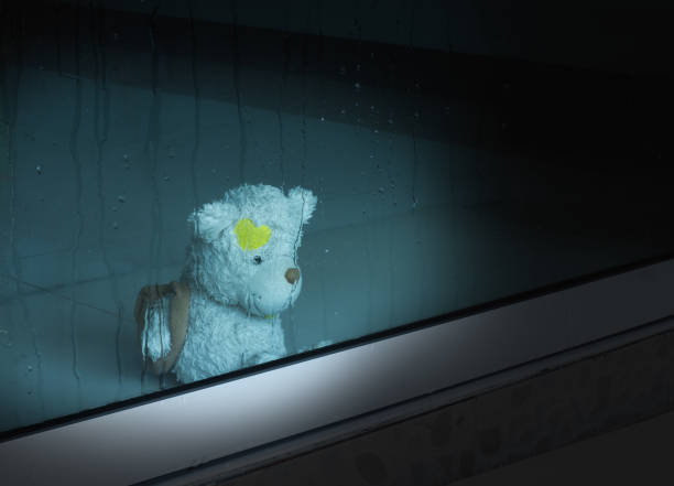 istock Teddy bear sit and looking through the window with  the window in rainy night day.broken heart concept.with copy space. 1273567562