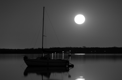 Sailboat under a full moon anchored in a mirror like lake
