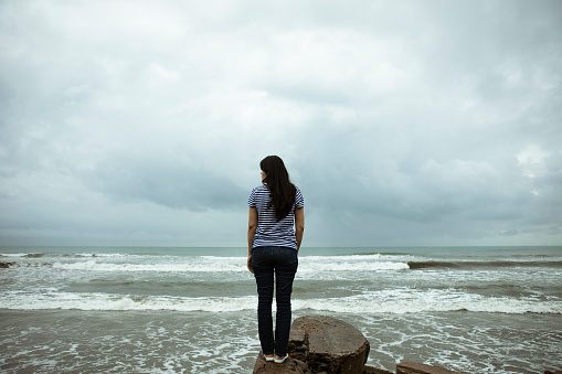 Sad and lonely woman standing in front of the Indian ocean and looking at the stormy water on Padang Beach, West Sumatra.
