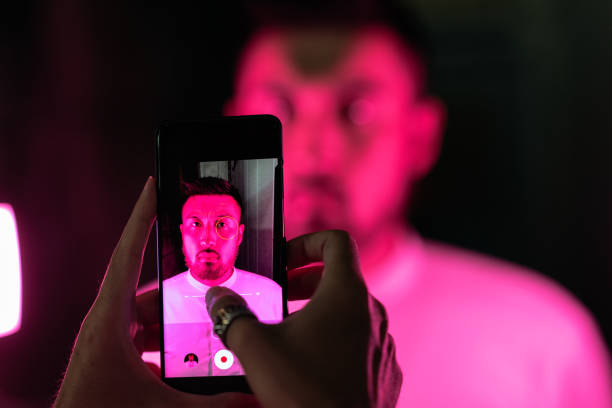 A young man is being filmed with a smart phone under pink neon light.