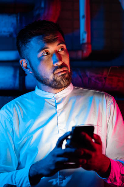 young man lit by pink and blue neon lights using smart phone at night in city - vertical bright brightly lit vibrant color imagens e fotografias de stock