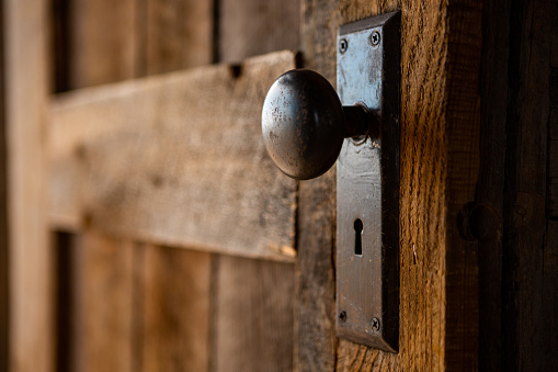 Outer Wooden door with old fashion knob and skeleton key hole with light reflecting off the metal of the door handle