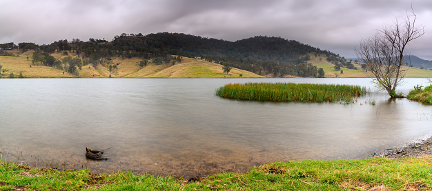 Scenic waterscape of Lostock Dam with an overcast sky and surrounding mountains and hillsides. At Lostock in the Upper Hunter of NSW, Australia.