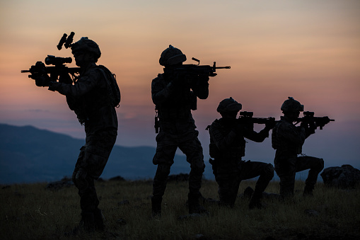 Israeli soldiers forming wearing IDF uniforms an L shape. Selective focus on a front gun barrel of an M-16A4 assault rifle.