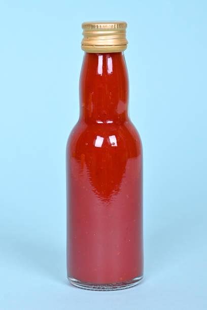 istock Hot red chilly sauce in little glass bottle on blue background. 1273601839