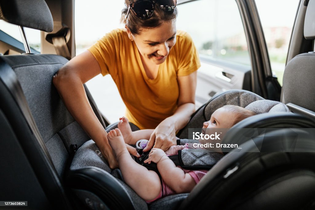 Mother putting baby girl in child seat in the car Mother putting baby girl in baby car seat Car Safety Seat Stock Photo