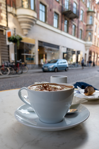 A fresh cup of hot chocolate of coffee in a white cup with saucer on streetside cafe table