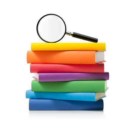 Stack of colored books with magnifying glass isolated on white background.