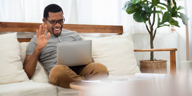 African American man sitting on sofa making online video call on laptop on sofa