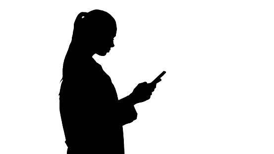Medium shot. Side view. Silhouette Cheerful cute young woman doctor typing text on phone while walking. Professional shot in 4K resolution. 013. You can use it e.g. in your commercial video, business, presentation, broadcast