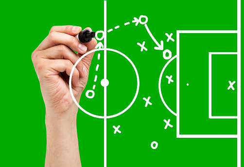 Coach drawing football or soccer game playbook, strategy and tactics with white marker on green background.
