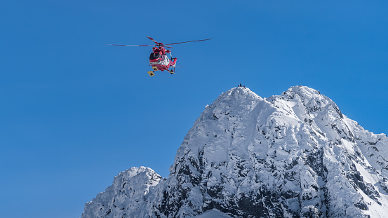 Rescue helicopter saved mountain climbers. People on the top of Swinica steep and rocky mountain peak at winter, Tatra Mountains, Poland