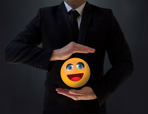 A businessman holding a smiling emoji between his two hands.