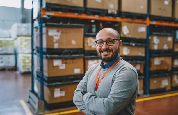 portrait of a smiling businessman standing in corridor of warehouse - warehouse box crate storage room imagens e fotografias de stock