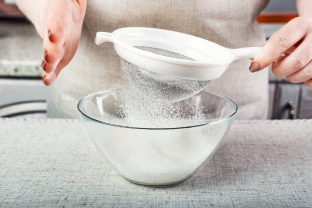 mãos do chef peneirar a farinha através de uma peneira em um recipiente de vidro - sifting - fotografias e filmes do acervo