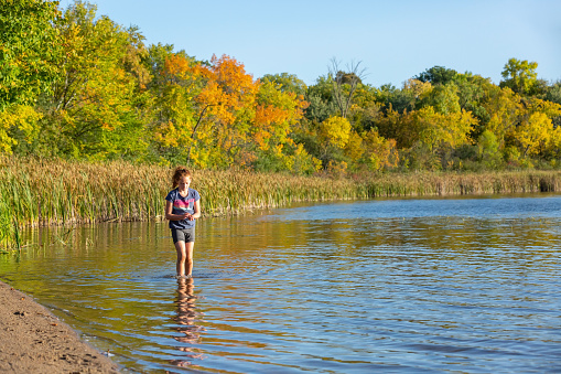 Girl walking in the shallow water at a small lake. She is holding small stones in her hand. Taken on a beautiful early autumn evening in Minnesota, USA.