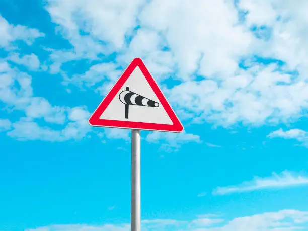 Road sign Crosswind. It is isolated on the blue sky with clouds.