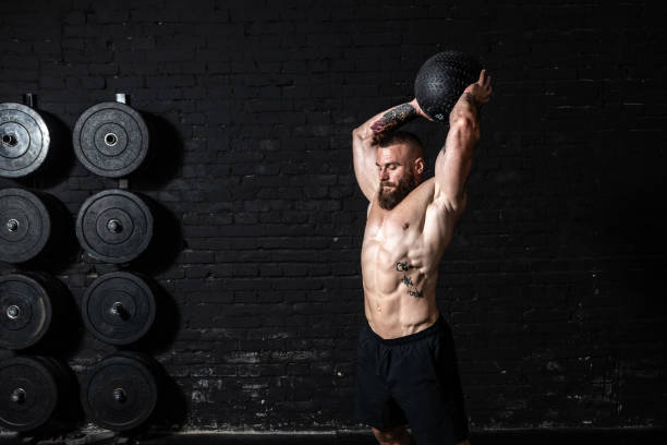 giovane uomo felato forte muscoloso con grandi muscoli che fanno palla lanciando sul pavimento come allenamento cross hardcore in palestra - botta grande foto e immagini stock