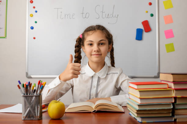 istock Cheerful pupil showing thumbs up gesture, studying at the classrom, reading a book 1273697604
