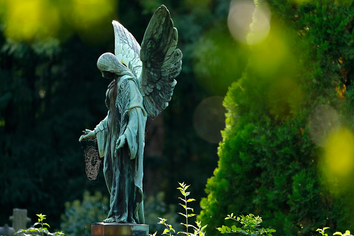 Weathered old copper angel statue with a spider web on a cemetery in Germany